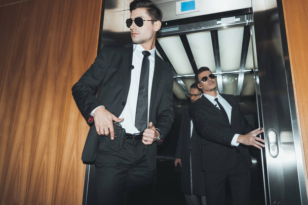guarda-costas colocando a mão na arma quando sair com homem de negócios do elevador
  - Foto, Imagem