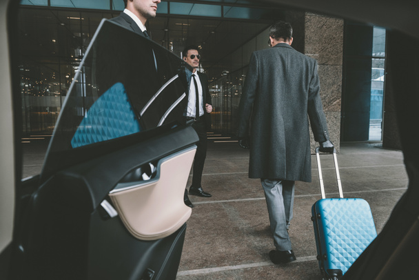 Geschäftsmann fährt mit blauer Tasche auf Rädern zum Flughafen   - Foto, Bild