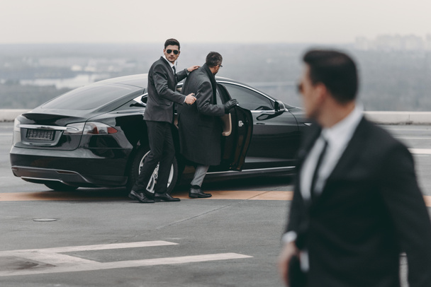 bodyguard helping businessman to sit in black car - Fotoğraf, Görsel
