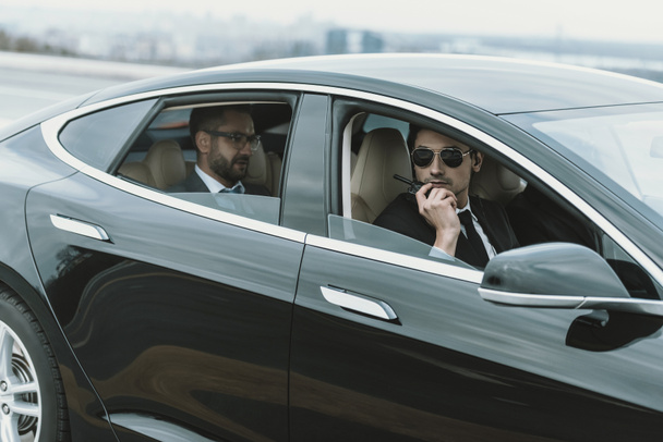 guarda-costas sentado no carro com empresário e falando por rádio portátil
 - Foto, Imagem