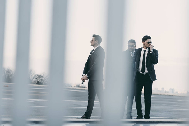 view through fence of businessman with bodyguards standing on helipad - Photo, Image