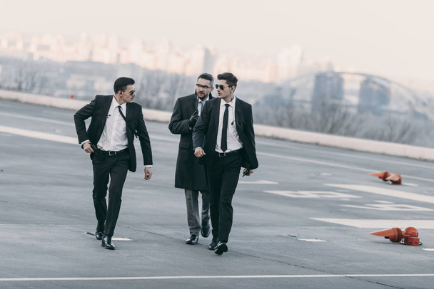 businessman walking with bodyguards in sunglasses and suits on helipad - Photo, Image