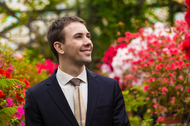 魅力的なフラワー ガーデンのビジネス スーツで若い男性の笑顔します。成功のコンセプト  - 写真・画像