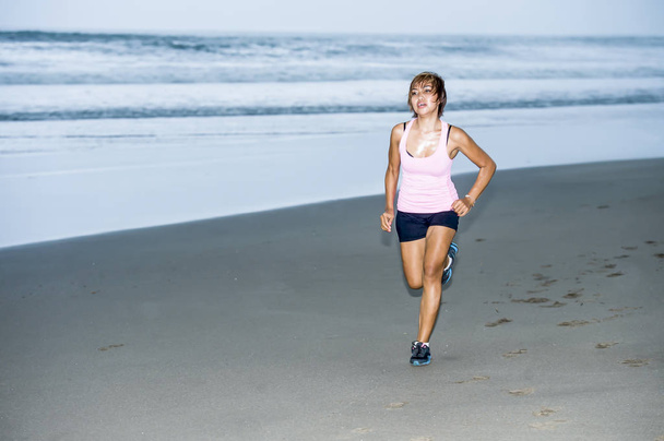 young attractive and fit Asian sport runner woman running on beach sea side looking tired while hard workout in fitness concept - Photo, Image