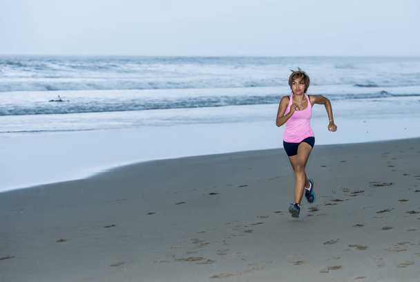 young attractive and fit Asian sport runner woman running on beach sea side smiling happy in fitness - Фото, изображение