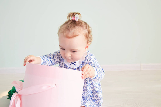baby girl opens the gift. pink box with bow - Foto, afbeelding