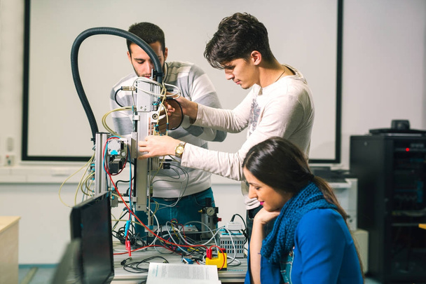 jovens estudantes felizes preparando robô para testes em oficina
 - Foto, Imagem