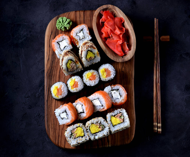 Sushi au wasabi et gingembre mariné sur une planche d'olivier sur fond de béton noir
. - Photo, image
