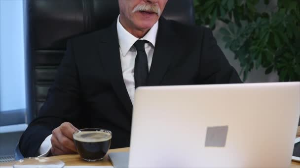 Businessman drinks coffe while watching the laptop screen - Кадри, відео