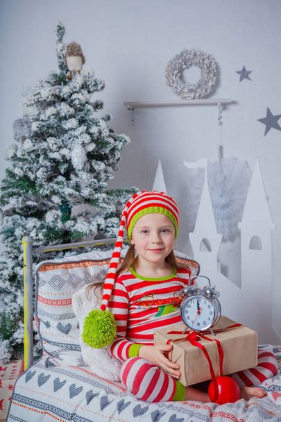 Happy cute little girl dressed in striped pajamas sitting in decorated New Year room at home. - Fotoğraf, Görsel