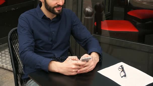 glücklicher Mann sitzt am Cafétisch und plaudert per Smartphone mit Großaufnahme in Zeitlupe. - Filmmaterial, Video