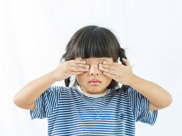 Egy aranyos kis lány kezét zárja be az egyik szeme, fehér háttér, - Fotó, kép