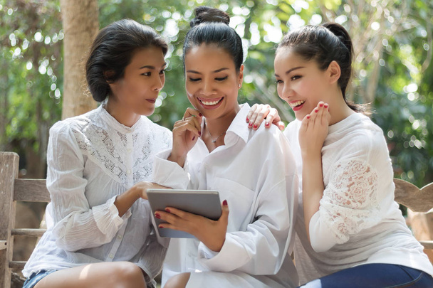 drei schöne Frauen sitzen mit einem Tablet in einem Park. - Foto, Bild