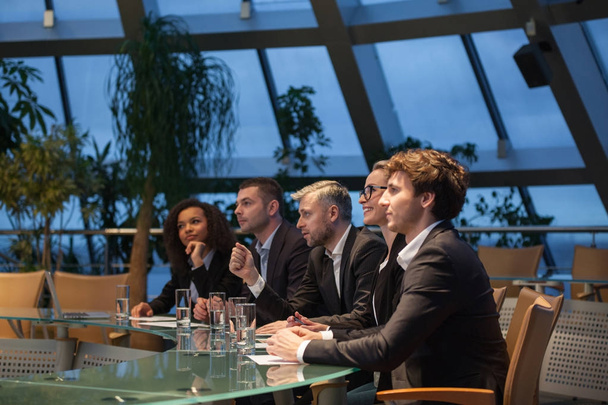 A group of business people sit at a table in a line and are discussing. - Foto, afbeelding