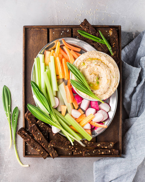 Traditional classic hummus of chickpeas, olive oil and spices. Served with fresh vegetables: celery, radishes, carrots, fresh green wild onions and whole grain bread crumbs. Useful dietary snack.  - Photo, Image
