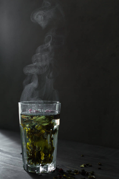 Hot mint tea with lemon, honey and berries in a glass is very good in the cold season with a rug and book. The steam from the tea is very beautiful) - Photo, Image