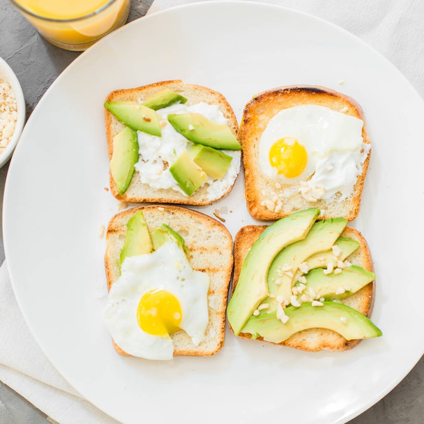 El desayuno. Huevos en tostadas con aguacate, queso blanco suave, especias y nueces. Placa blanca, fondo de hormigón gris
. - Foto, Imagen