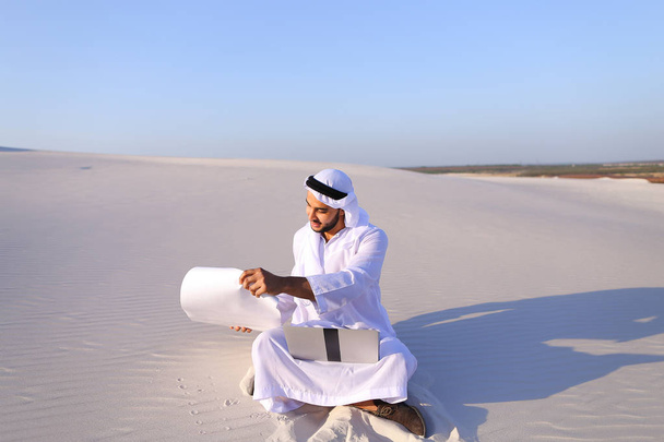 H üzerinde çölde kum üstünde laptop ile oturan Müslüman erkek mimar - Fotoğraf, Görsel