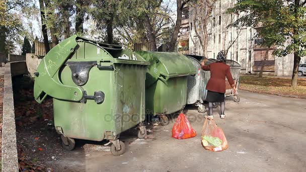 Dakloze vrouw is op zoek naar voedsel in de afval container. Vrouw in armoede is iets zoeken in container. - Video