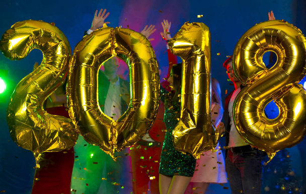 The composition of the golden balloons in the form of figures on a background of a dancing group of young people. The new year 2018. Festive New Year party or disco. - Fotoğraf, Görsel
