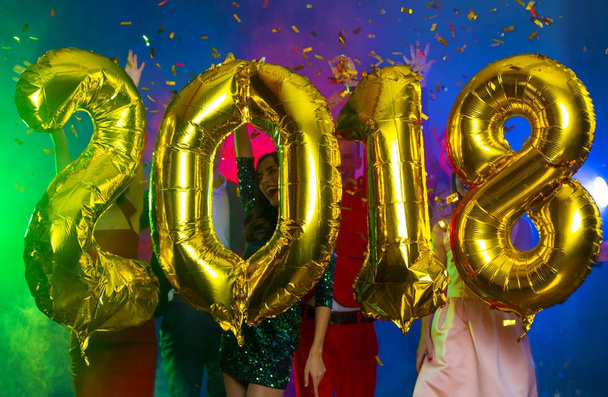 The composition of the golden balloons in the form of figures on a background of a dancing group of young people. The new year 2018. Festive New Year party or disco. - Foto, Imagen