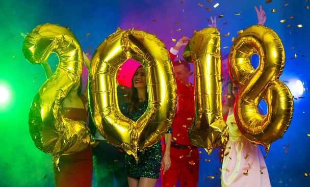 Η σύνθεση του golden μπαλόνια με τη μορφή των αριθμών με φόντο ένα χορευτικό συγκρότημα νέων ανθρώπων. Το νέο έτος 2018. Εορταστικό πρωτοχρονιάτικο πάρτι ή ντίσκο. - Φωτογραφία, εικόνα