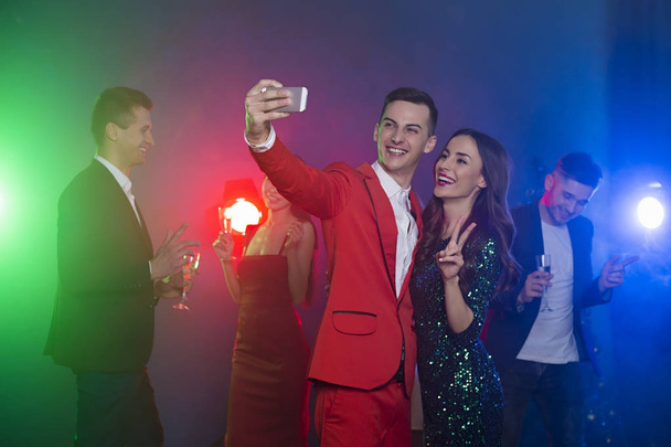 Friends rest and dance in the club on holiday. The guy with the girl do selfie on the phone - Foto, imagen