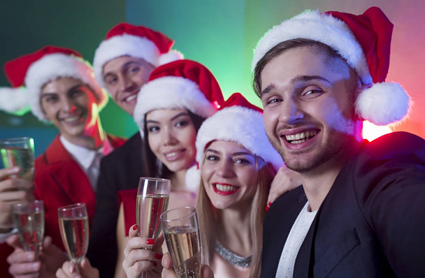 Group of smiling friends in Santa hats are photographed or make selfie on New Year's party - Φωτογραφία, εικόνα
