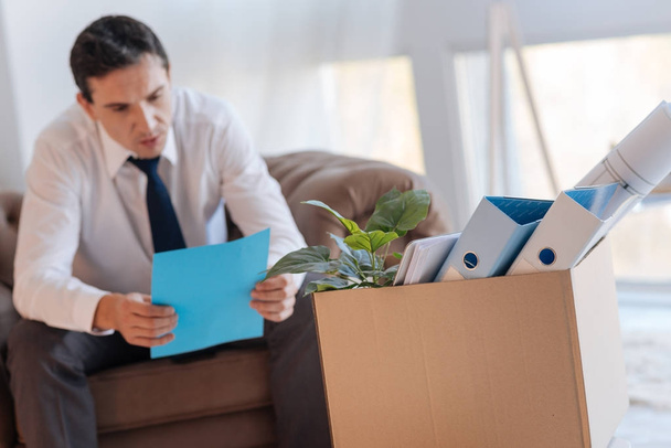 Calm elegant man reading a document while sitting in front of a big box - Photo, Image
