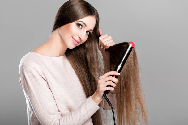 woman ironing hair with hair iron. - Фото, изображение