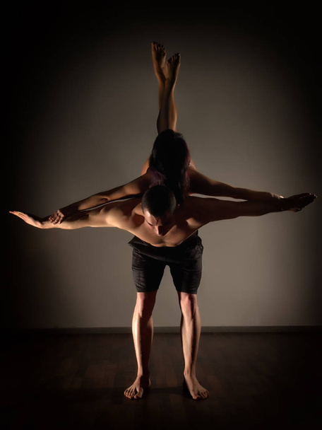 sports man and woman doing acroyoga exercises in a dark room - 写真・画像