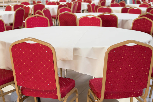 Cadeiras vermelhas lascadas com têxteis e mesas com toalha de mesa branca
 - Foto, Imagem