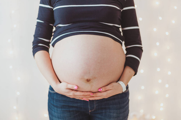 Close-up of pregnant womans big hairy belly on bright bokeh lights background - Foto, immagini