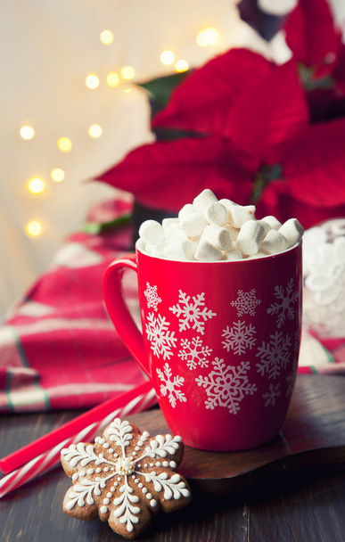 Close-up of a mug with a hot drink, marshmallow and gingerbread. Christmas decor with a bright garland and fir tree. Selective focus, shallow depth of field, background - Fotó, kép
