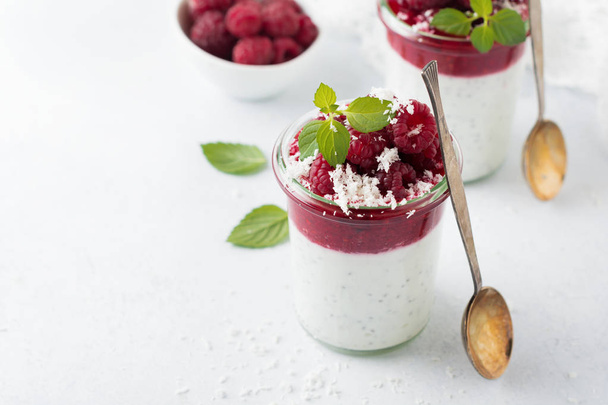 Layered raspberry smoothies with chia seeds, fresh raspberry and coconut on a light stone background. Useful dessert. Selective focus. - Foto, Bild