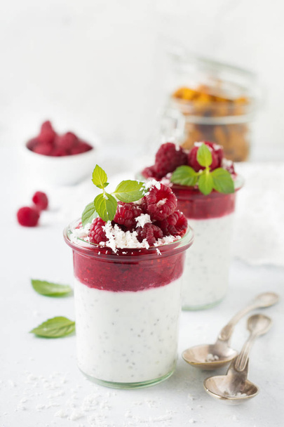 Layered raspberry smoothies with chia seeds, fresh raspberry and coconut on a light stone background. Useful dessert. Selective focus. - Foto, imagen