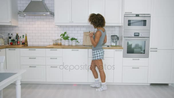 Young woman dancing in kitchen with smartphone - Filmmaterial, Video