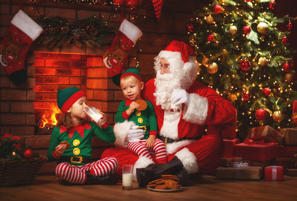 Navidad. Santa Claus con elfos beben leche y comen galletas
 - Foto, imagen