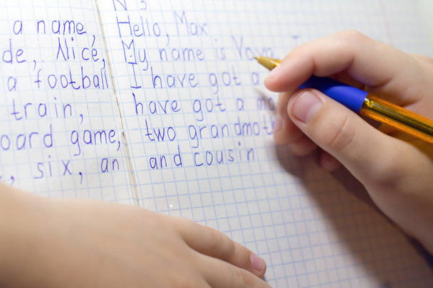 伝統的な白いメモ帳の紙に手で英単語を書く鉛筆と少年の手のクローズ アップ. - 写真・画像