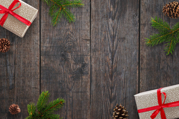 Рождественский фон с подарками, еловыми ветвями и шишками над черным деревянным столом. Вид сверху
. - Фото, изображение