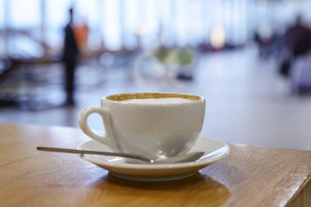 taza de café caliente capuchino en una taza blanca está sobre la mesa en el vestíbulo del aeropuerto
 - Foto, Imagen