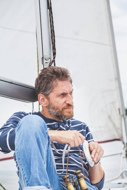 man with beard sits on deck of sailing yacht - Φωτογραφία, εικόνα