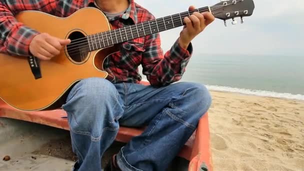 Hombre tocando la guitarra sentado en un barco en la playa
 - Imágenes, Vídeo