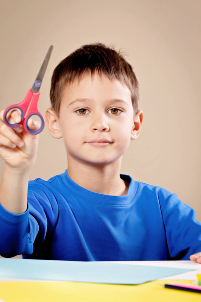 Boy cutting colored paper with scissors at the table - Foto, Bild