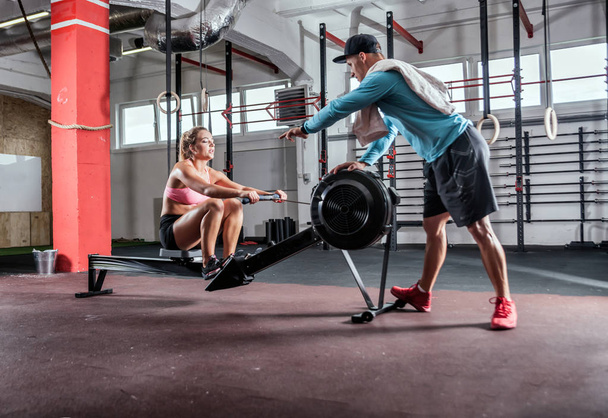 Girl training on row machine with assistance of trainer at gym - Fotoğraf, Görsel