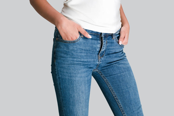 Ідеальні джинси. Крупним планом частина молодої жінки тримає руки в кишенях, стоячи на білому тлі
 - Фото, зображення
