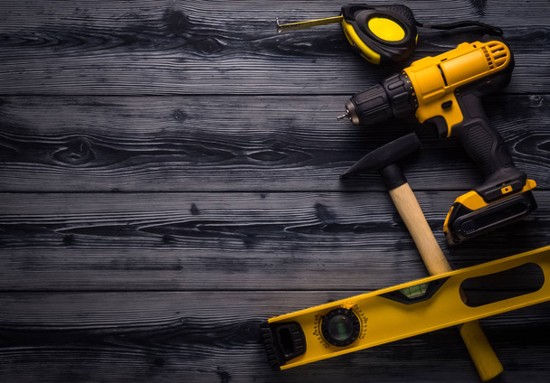 Yellow drill, hammer, level and a roulette on wooden background - Fotoğraf, Görsel