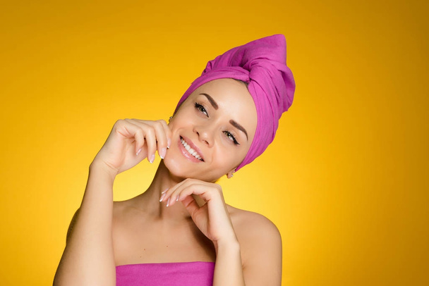 happy young girl with a pink towel on her head looks after the face, smiling - Foto, Imagen