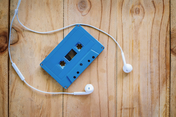 Blue retro cassette tape and white earphone on wooden table, added color filler and soft tone - Foto, Bild
