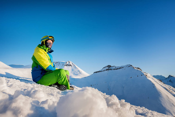 Girl traveler in a ski suit sits in the snow against the backgro - Φωτογραφία, εικόνα